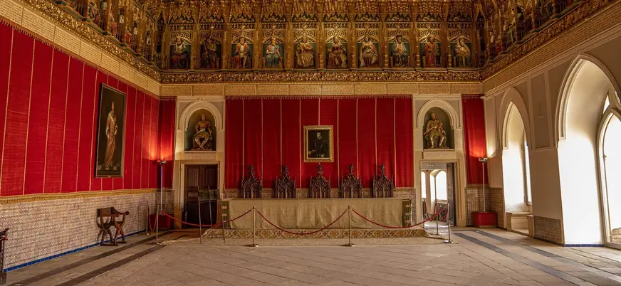 Sala del Trono en el Alcázar de Segovia con friso de reyes y tapices rojos.