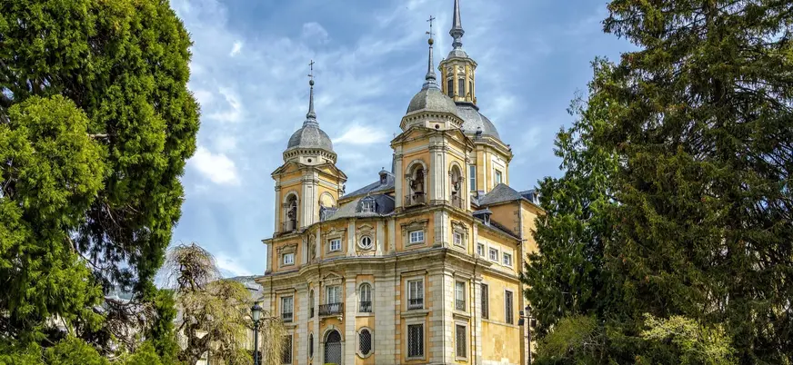 Colegiata del Palacio Real de La Granja de San Ildefonso entre árboles verdes.
