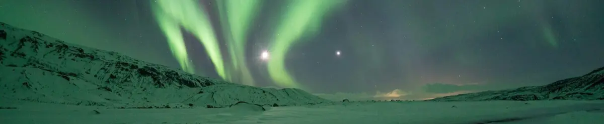 Aurora boreal sobre un paisaje nevado en Islandia, con reflejos verdes iluminando el cielo y las montañas.
