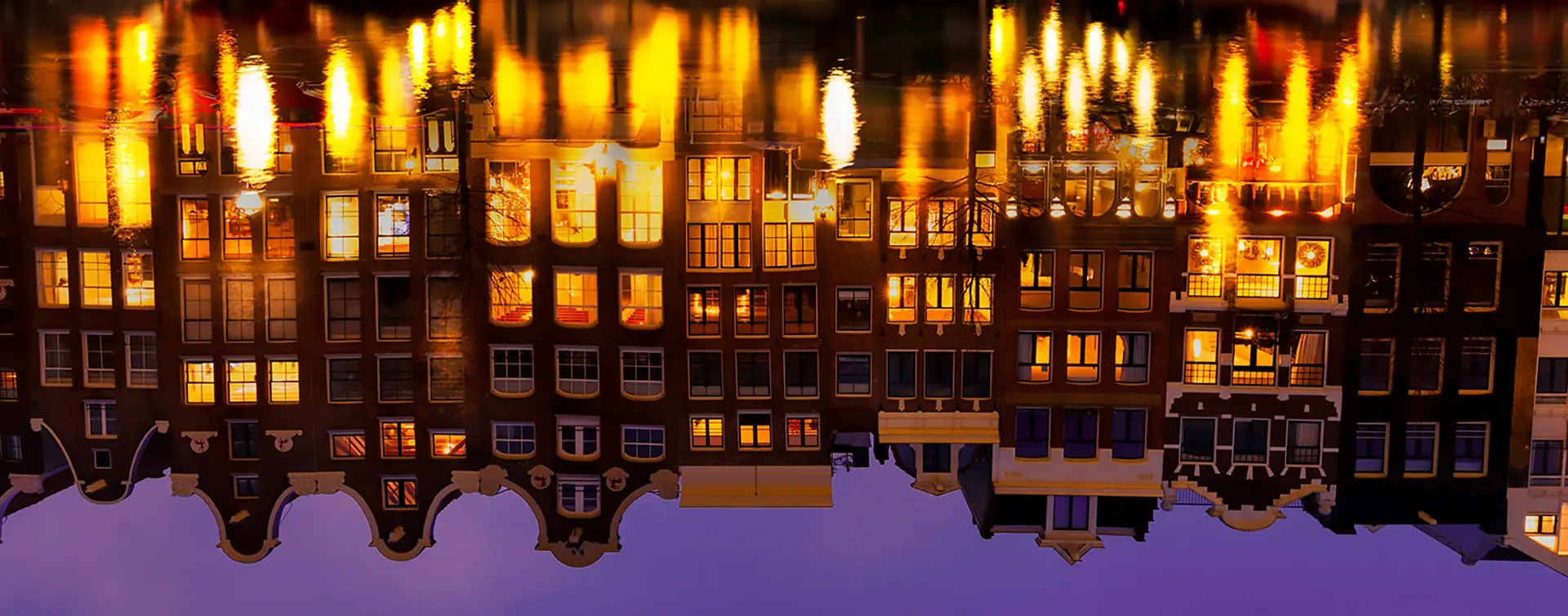Reflejo en el agua de casas iluminadas de noche visto desde un crucero en los canales de Amsterdam - Tour nocturno por los canales de Ámsterdam - Buendía Tours Países Bajos - Holanda