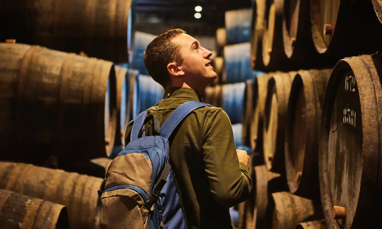 Visitante recorriendo una bodega tradicional entre barricas de vino en Oporto.