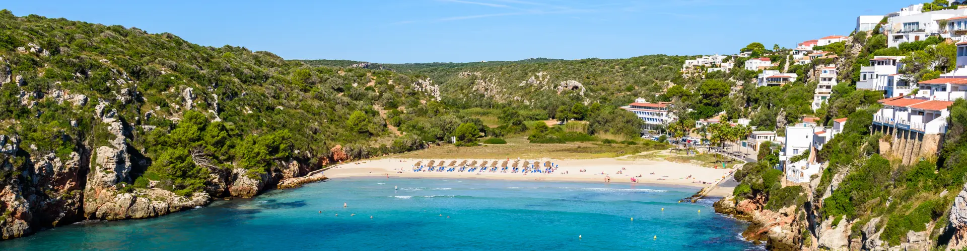 Encantadora Cala Porter, una playa de aguas turquesas rodeada de acantilados y vegetación en Menorca.