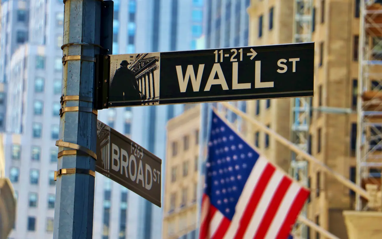 Señal de Wall Street y Broad Street con banderas estadounidenses y edificios del distrito financiero de Nueva York.