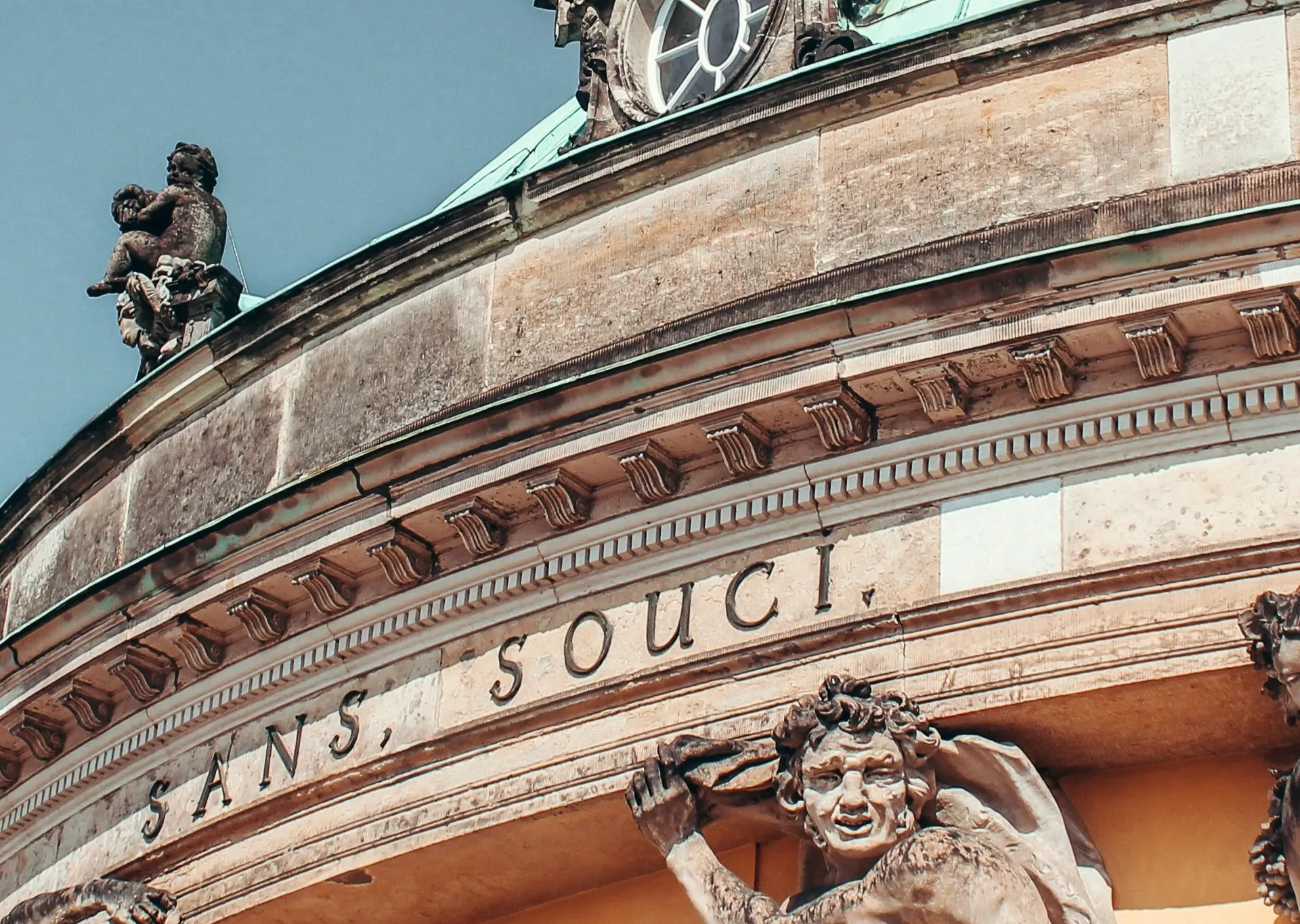 Detalle de la fachada del Palacio de Sanssouci en Potsdam, con estatuas de atlantes, inscripciones y la cúpula verde.