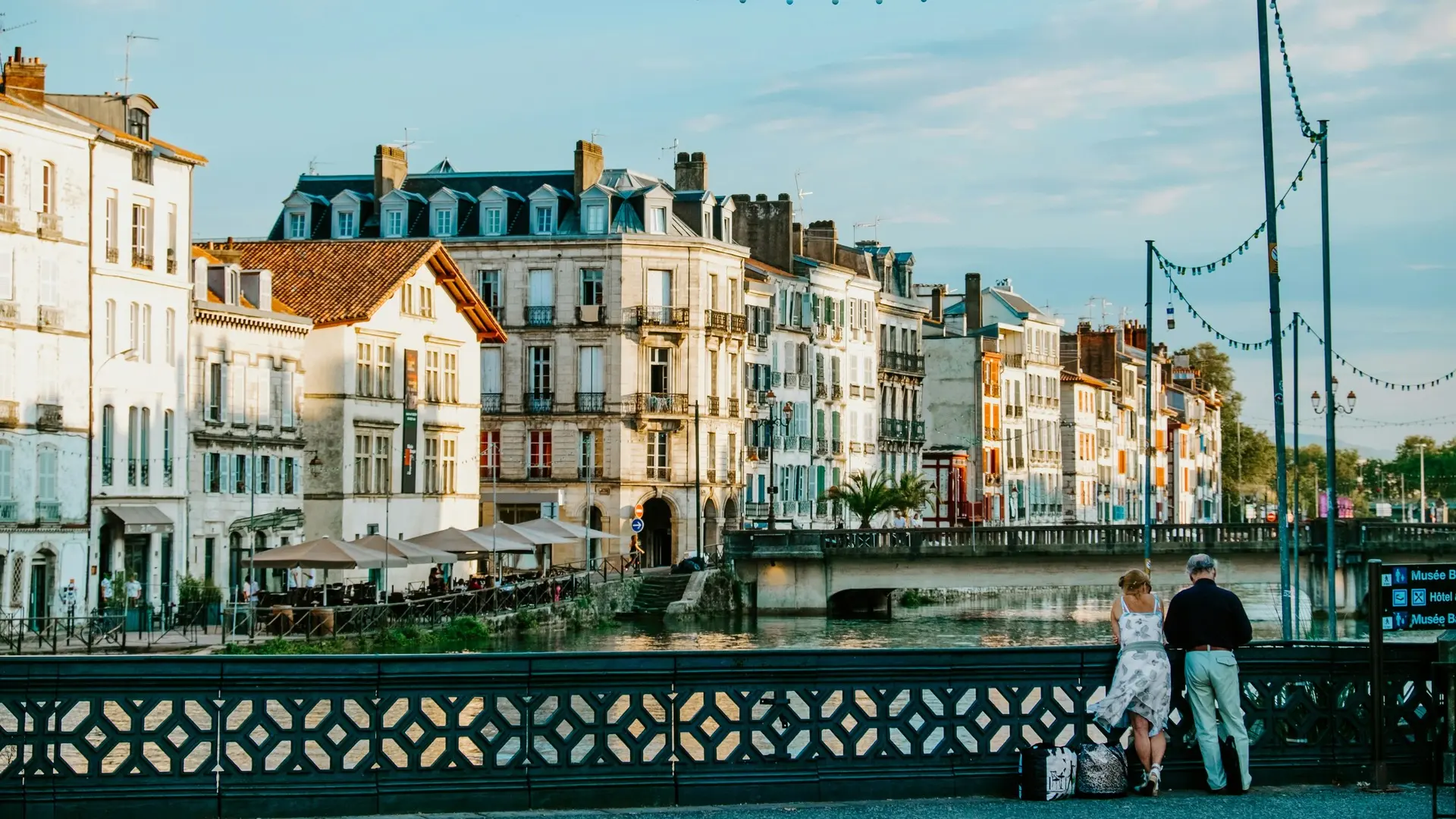 Río y casas al atardecer en Bayona, con parejas apoyadas en el puente.