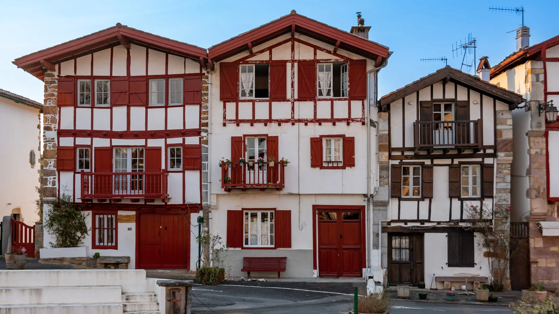 Fachadas típicas de casas vascas con madera roja y balcones floridos en el centro histórico de Espelette.