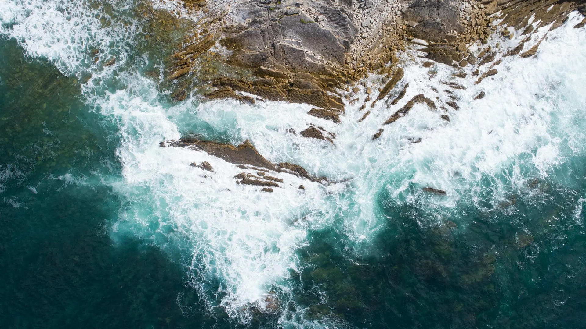 Vista aérea de las olas turquesas rompiendo contra las rocas y el acantilado en la costa de San Juan de Luz.