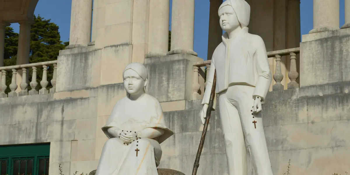 Estatua de los pastores Francisco y Jacinta Marto en Fátima, Portugal, sobre pedestal con columnas detrás.