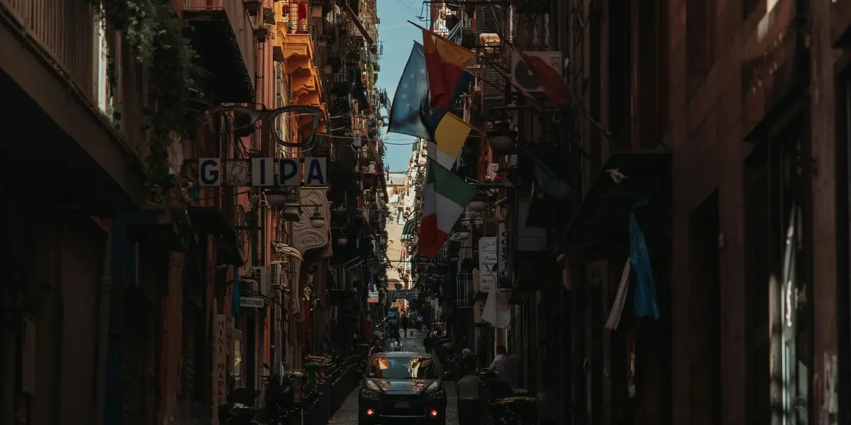 Calle estrecha y oscura de los Quartieri Spagnoli (Barrios Españoles) en Nápoles, Italia, con banderas colgantes.