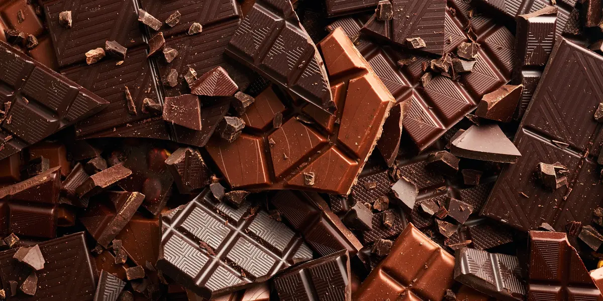 Primer plano de tabletas y trozos de chocolate negro y con leche, de Astorga o artesanal, apilados en textura densa.