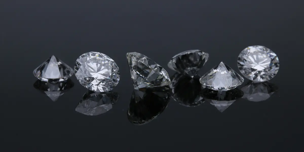 Primer plano de varios diamantes de talla brillante y puntas sobre una superficie oscura, reflejando luz con brillo intenso.