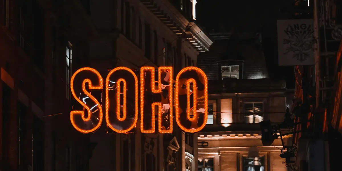 Letrero neón naranja con la palabra SOHO en una calle nocturna de Londres.