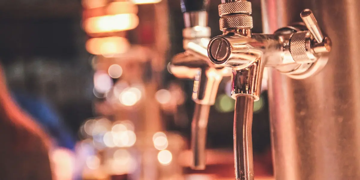 Grifos de cerveza metálicos en primer plano con bar de Berlín desenfocado.