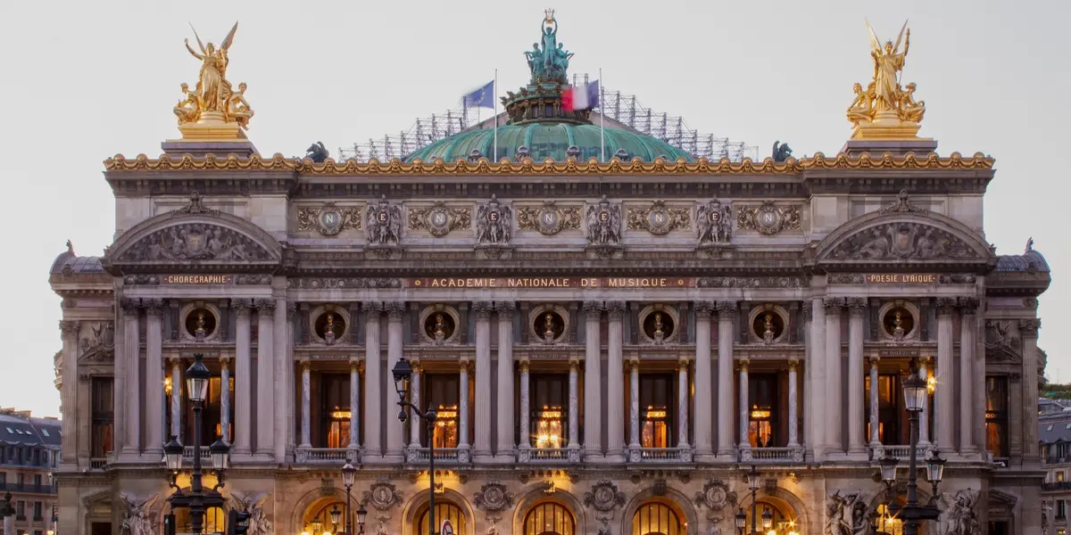 Fachada iluminada de la Ópera Garnier bajo el cielo del atardecer en París.
