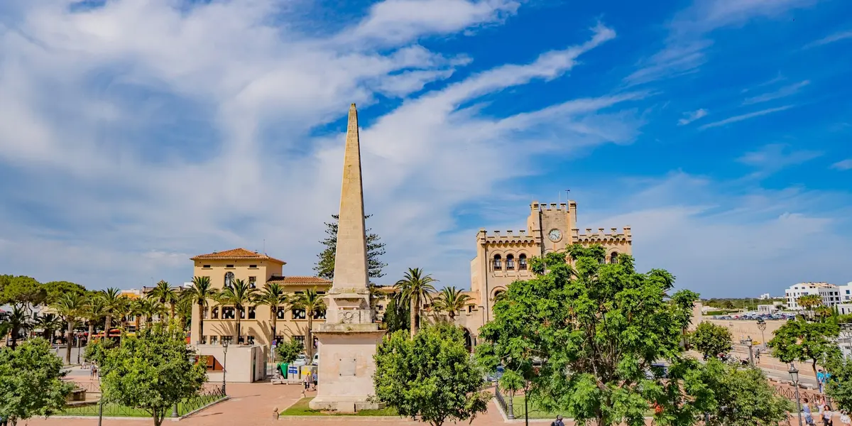 Obelisco en la Plaça des Born de Ciutadella frente al ayuntamiento y palmeras.