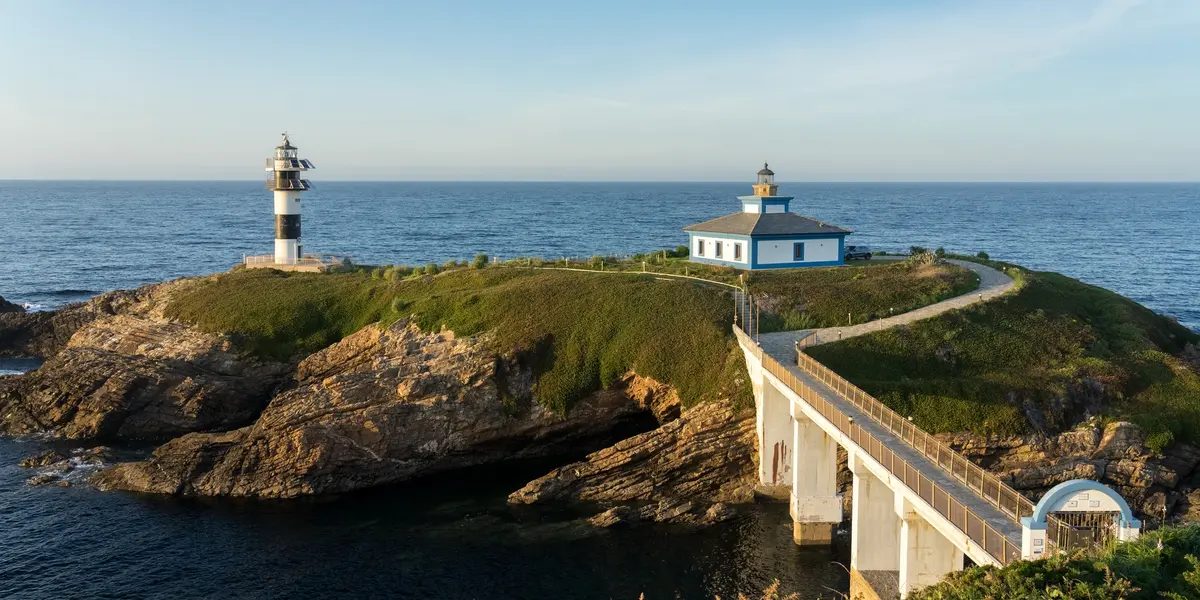 Faro de la Isla Pancha en Lugo, conectado por un puente a la costa. Edificio y torre blanca y negra junto al mar.