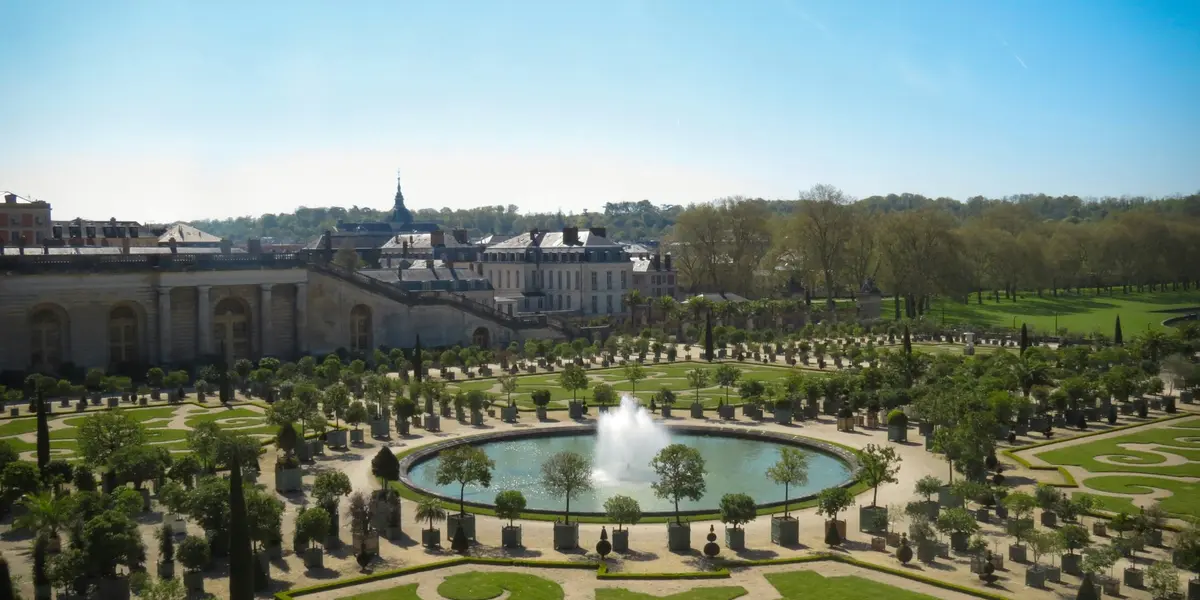 Jardines de Versalles, con fuentes, caminos simétricos y exuberante vegetación bajo un cielo despejado.