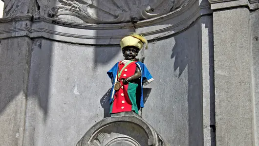 Estatua del Manneken Pis con traje típico multicolor en su fuente de Bruselas