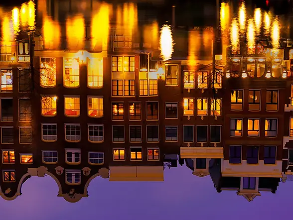 Reflejo en el agua de casas iluminadas de noche visto desde un crucero en los canales de Amsterdam - Tour nocturno por los canales de Ámsterdam - Buendía Tours Países Bajos - Holanda