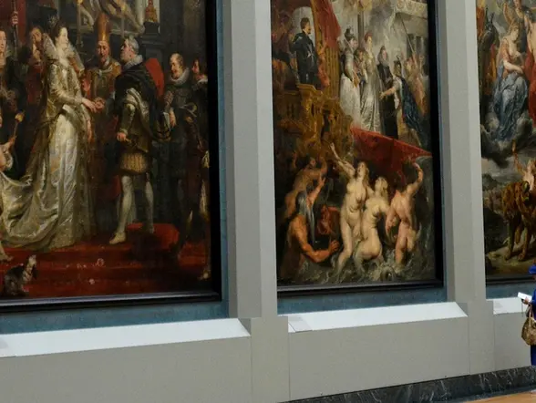 Mujer con vestido azul observa pinturas en el Museo del Louvre.