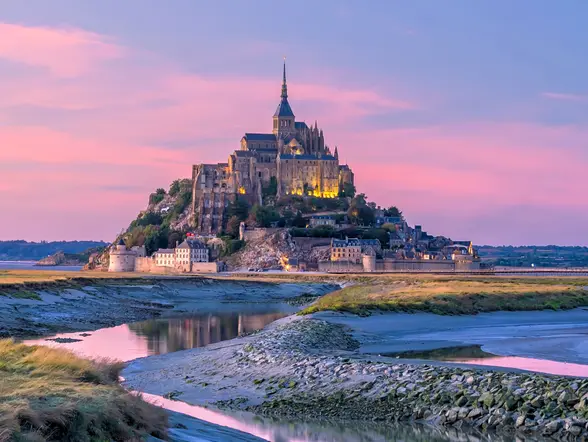 Mont Saint-Michel al atardecer en Normandía, Francia, abadía medieval rodeada de praderas y canales.