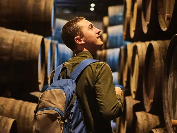 Visitante recorriendo una bodega tradicional entre barricas de vino en Oporto.