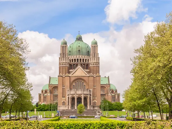 Fachada de la Basílica del Sagrado Corazón de Bruselas rodeada de árboles y jardines.