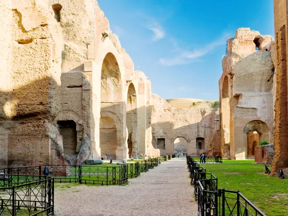 Ruinas de las Termas de Caracalla en Roma, con grandes muros de ladrillo, arcos monumentales y áreas verdes bajo cielo despejado.