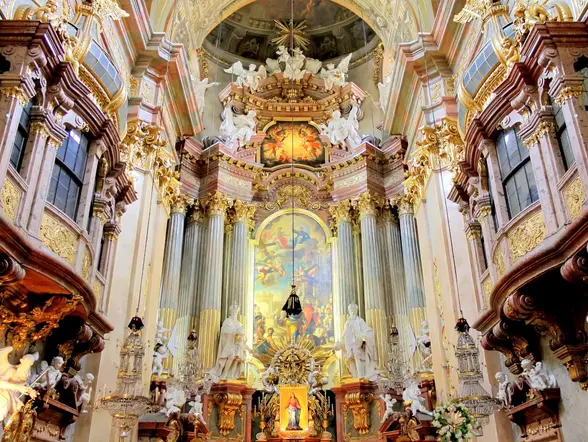 Interior barroco muy ornamentado de la Iglesia de San Pedro en Viena, con un altar dorado, esculturas y una gran pintura central.