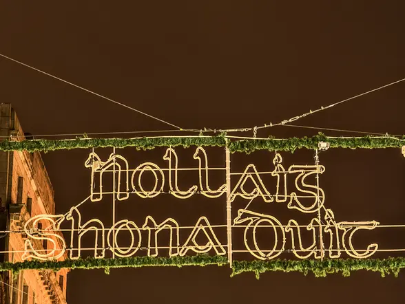 Cartel luminoso colgado en la calle con la frase 'Nollaig Shona Duit', decoración navideña en irlandés, durante la noche.