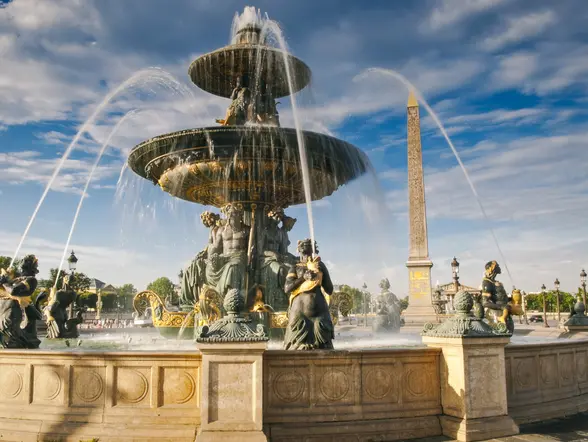 Fuente histórica en París con estructura de piedra y detalles arquitectónicos rodeada de vegetación.