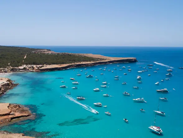 Cala Saona vista desde lo alto, con barcos, vegetación y aguas de un azul intenso.