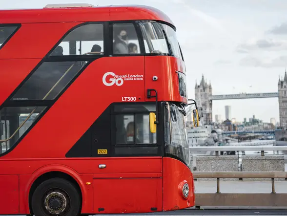Autobús rojo de dos pisos cruzando Londres con el Puente de la Torre al fondo, típico del transporte londinense.