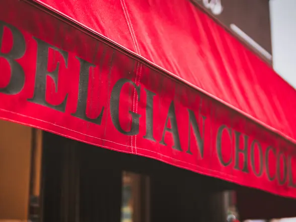 Toldo rojo de tienda con el texto "BELGIAN CHOCOLATE" en letras grandes y negras, anunciando chocolates belgas.