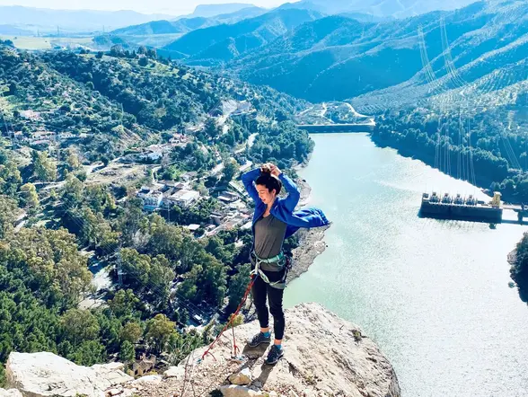 Mujer con arnés en la cima de El Chorro con vistas al embalse y al pueblo.