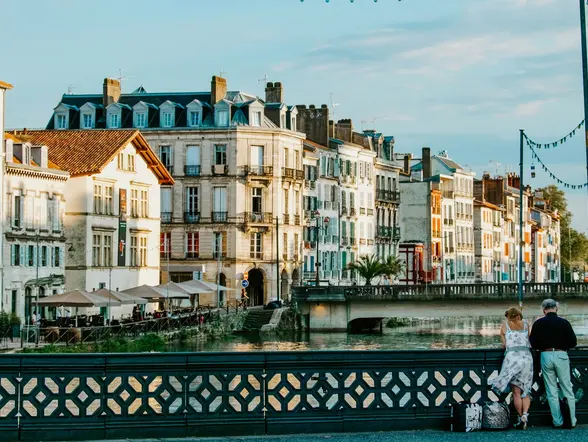 Río y casas al atardecer en Bayona, con parejas apoyadas en el puente.
