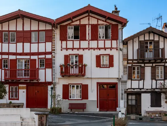 Fachadas típicas de casas vascas con madera roja y balcones floridos en el centro histórico de Espelette.