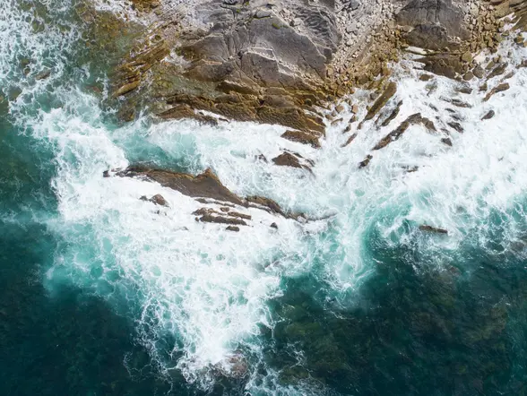 Vista aérea de las olas turquesas rompiendo contra las rocas y el acantilado en la costa de San Juan de Luz.