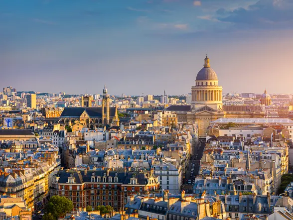Ciudad de París al atardecer, mostrando un horizonte con edificios emblemáticos y un cielo teñido de tonos cálidos.