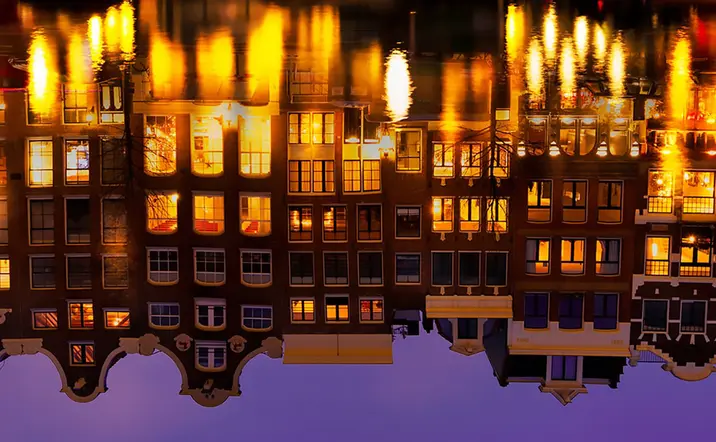 Reflejo en el agua de casas iluminadas de noche visto desde un crucero en los canales de Amsterdam - Tour nocturno por los canales de Ámsterdam - Buendía Tours Países Bajos - Holanda