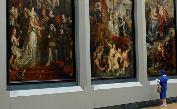 Mujer con vestido azul observa pinturas en el Museo del Louvre.