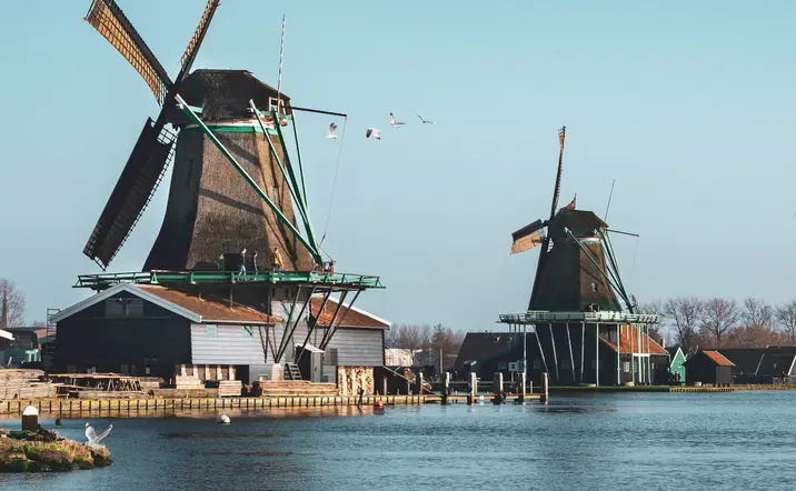 Vista panorámica de varios molinos de viento tradicionales alineados junto a un canal en Zaanse Schans, Países Bajos.