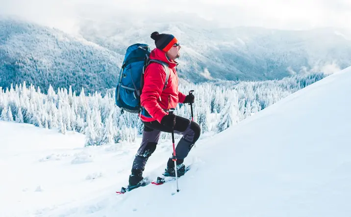 Hombre con chaqueta roja y mochila haciendo una ruta en raquetas de nieve por Sierra Nevada - Ruta en Raquetas de Nieve por Sierra Nevada - Actividades,  Experiencia al aire libre, Ocio y Turismo activo Buendía Andalucía 