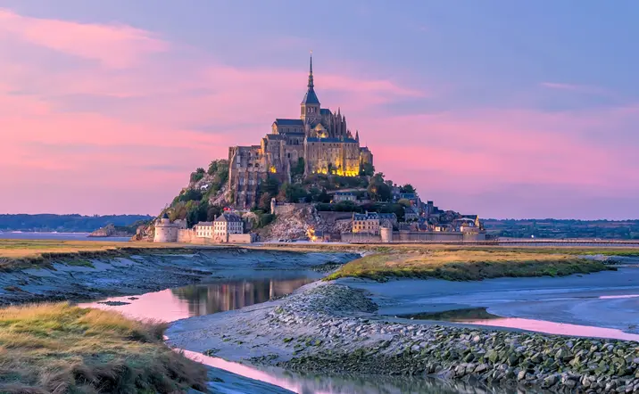 Mont Saint-Michel al atardecer en Normandía, Francia, abadía medieval rodeada de praderas y canales.