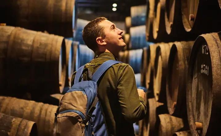 Visitante recorriendo una bodega tradicional entre barricas de vino en Oporto.