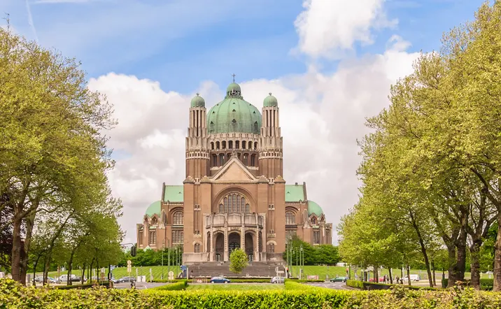 Fachada de la Basílica del Sagrado Corazón de Bruselas rodeada de árboles y jardines.