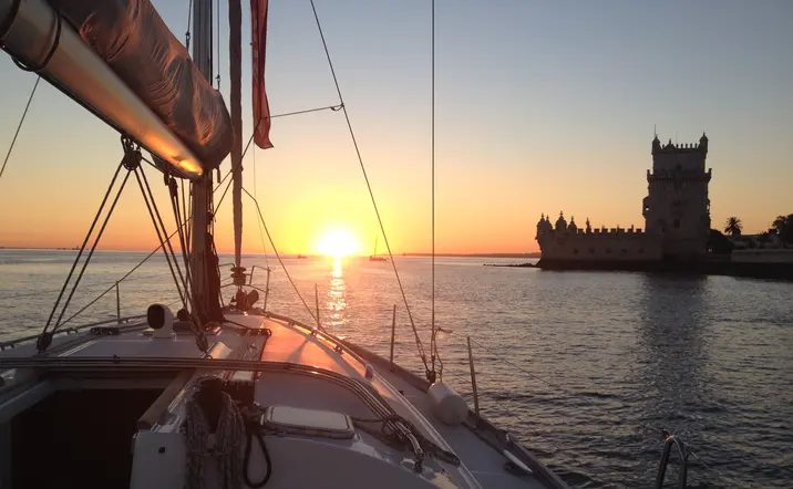 Puesta de sol sobre el río Tajo vista desde un velero, con la Torre de Belém al fondo en Lisboa.
