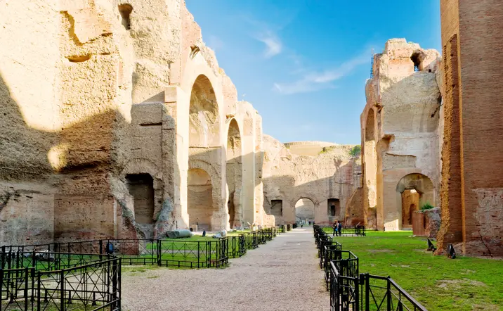 Ruinas de las Termas de Caracalla en Roma, con grandes muros de ladrillo, arcos monumentales y áreas verdes bajo cielo despejado.