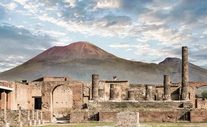 Ruinas de Pompeya con el imponente monte Vesubio al fondo, mostrando columnas y estructuras romanas preservadas por la erupción volcánica del año 79 d.C.