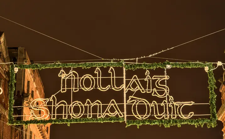 Cartel luminoso colgado en la calle con la frase 'Nollaig Shona Duit', decoración navideña en irlandés, durante la noche.